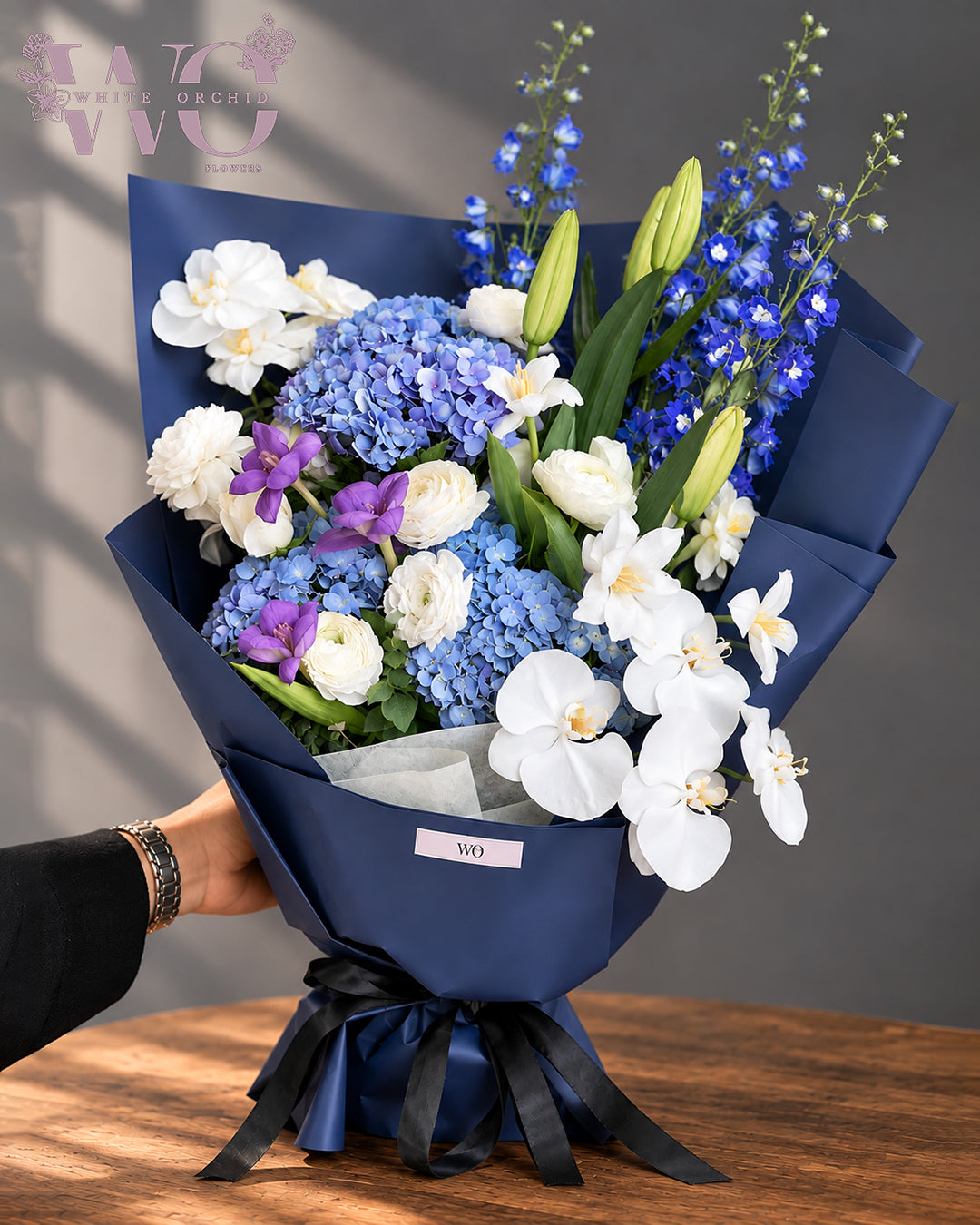 Luxury blue and white bouquet with hydrangeas, white orchids and lilies in navy wrapping