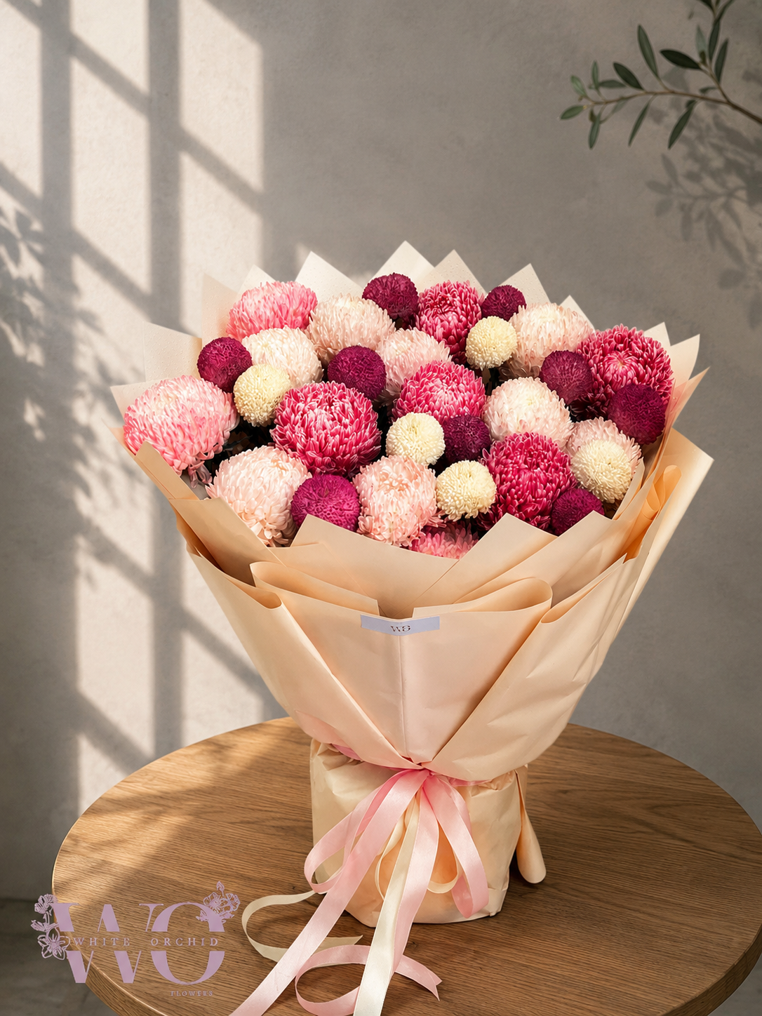 Luxury pink and white chrysanthemum hand bouquet wrapped in champagne paper with a pink ribbon