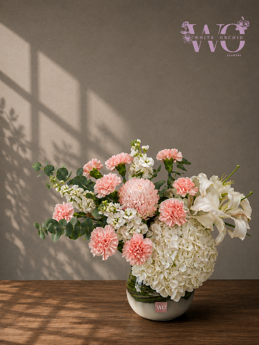 Peach and white floral arrangement with carnations, hydrangeas, lilies and eucalyptus in a glass vase by White Orchid Flowers