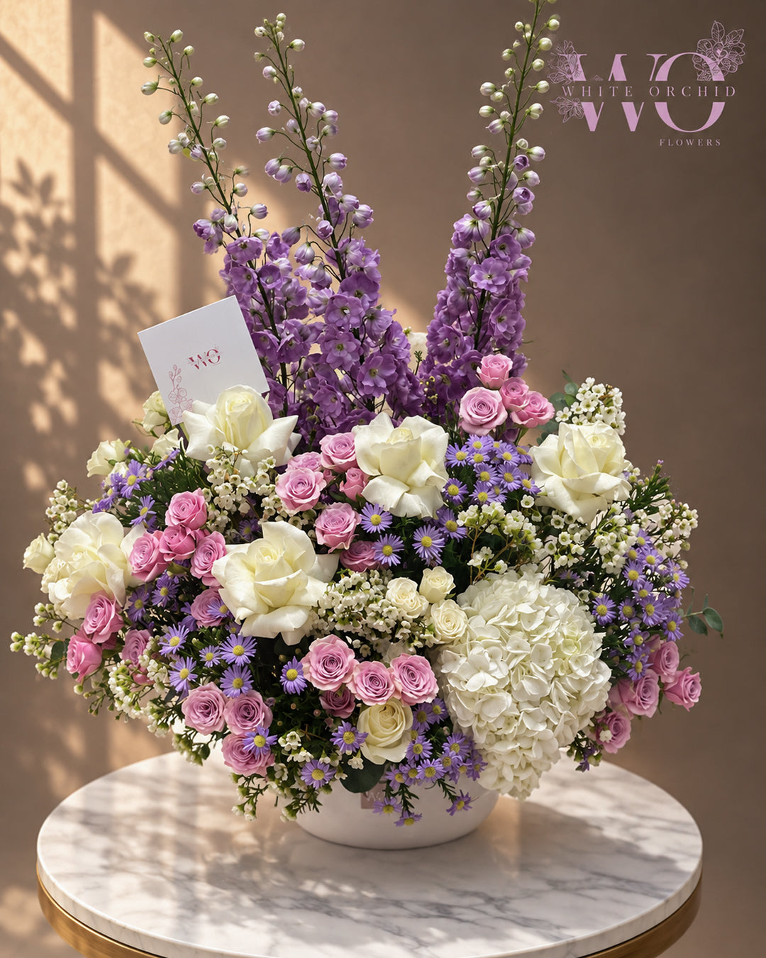 Purple and white luxury floral arrangement with roses, hydrangeas and purple flowers in a white vase by White Orchid Flowers