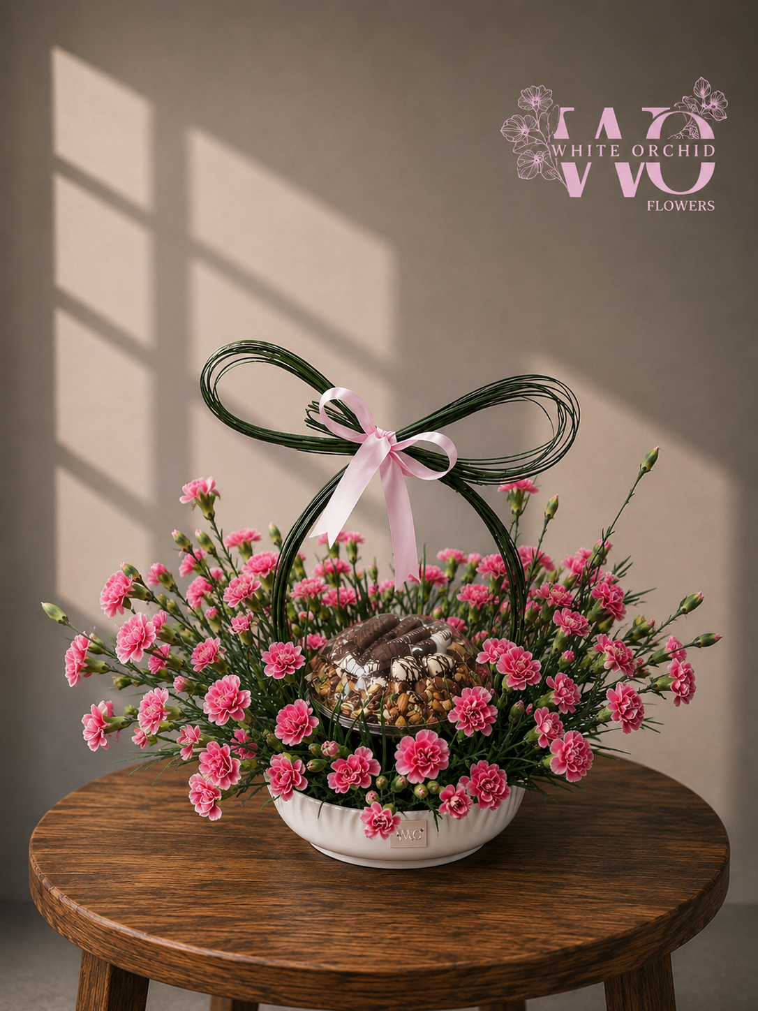 Pink carnation flower arrangement with chocolate gift in an elegant white bowl