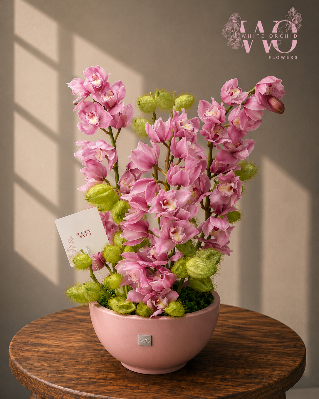 Pink orchid flower arrangement with green botanicals in an elegant pink ceramic bowl