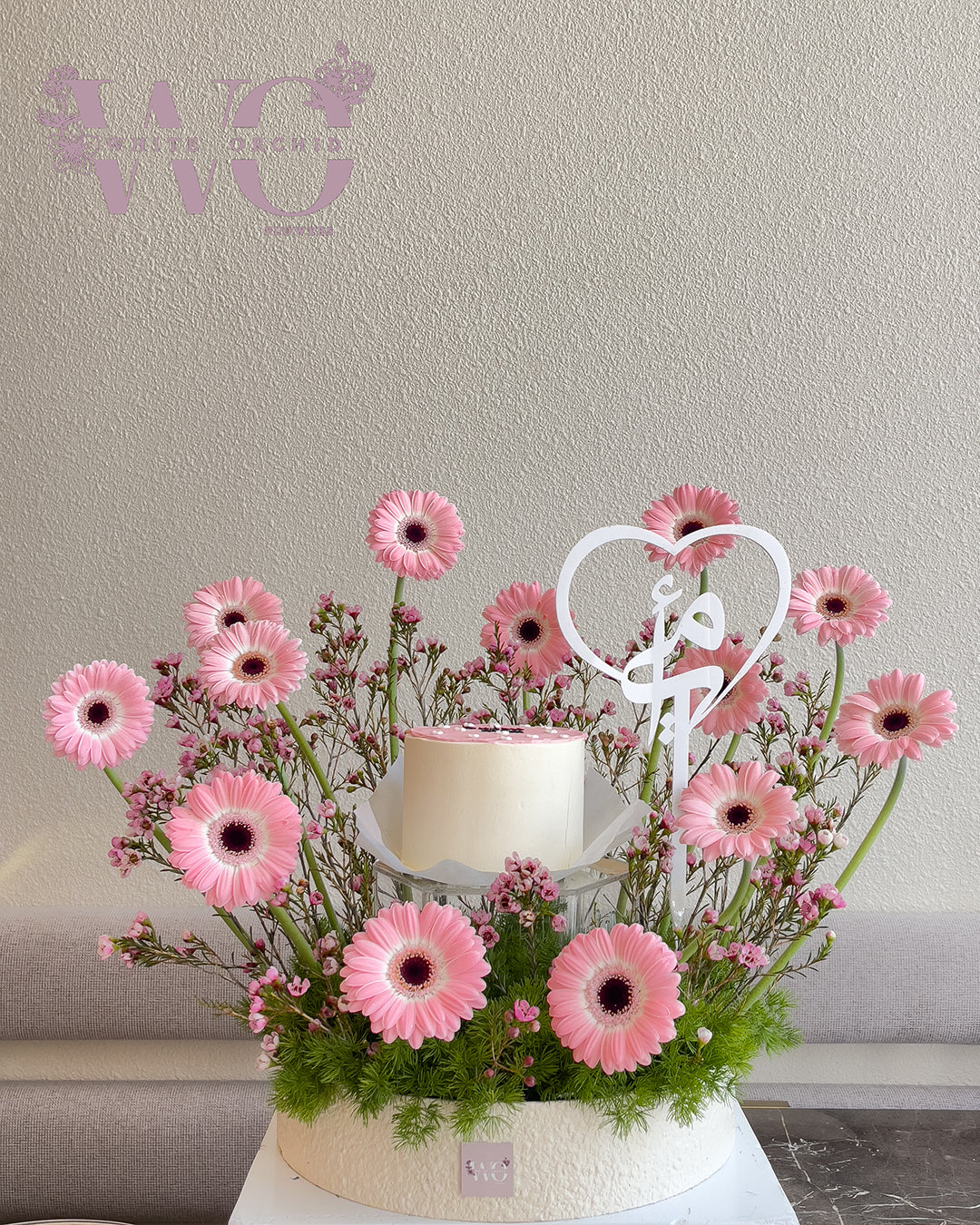 Mother’s Day flower arrangement with pink gerbera flowers and cake with heart detail by White Orchid Flowers UAE.