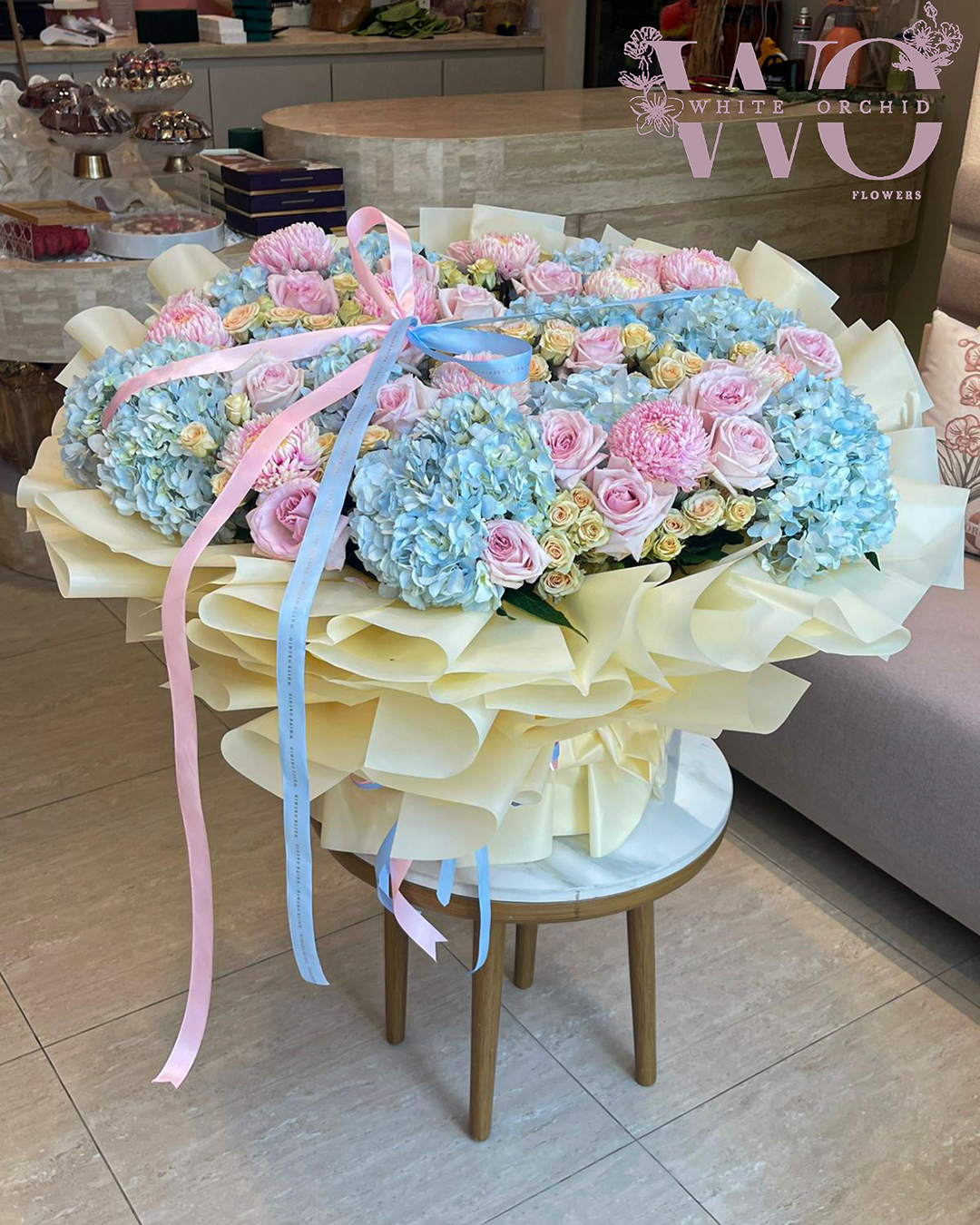 Luxury bouquet with blue hydrangeas, pink roses, spray roses, and chrysanthemums wrapped in elegant packaging.