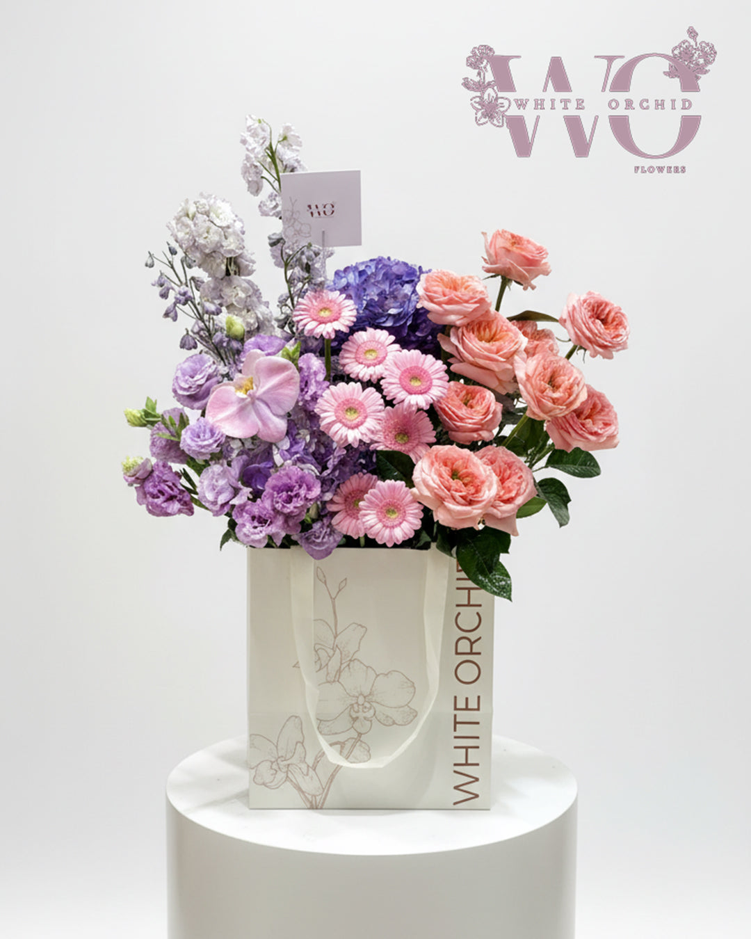 Pastel mixed flower hand bouquet with roses, gerbera, and hydrangea in a luxury White Orchid bag.