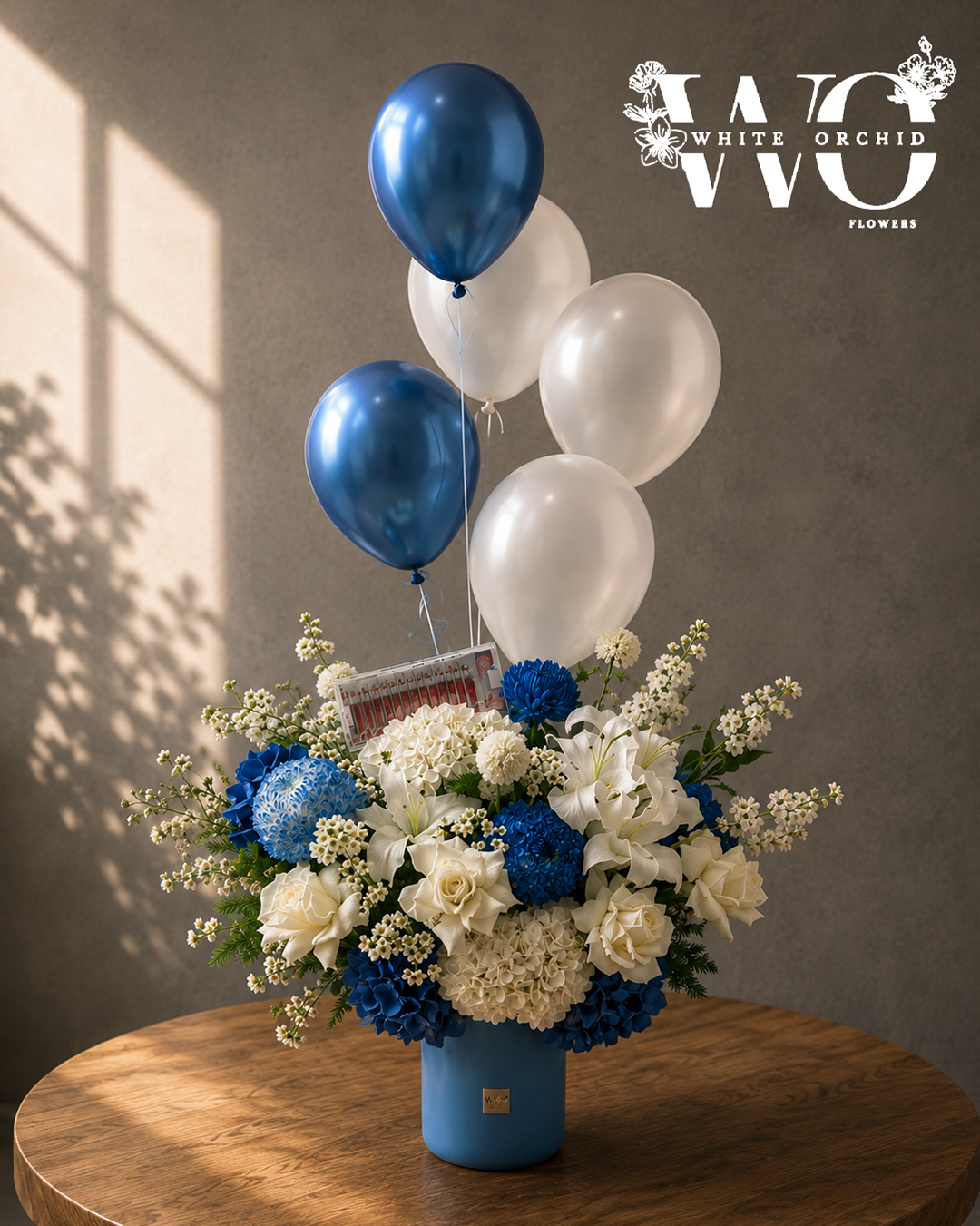 Baby boy blue and white flower arrangement with roses, lilies, hydrangeas and balloons in a blue vase